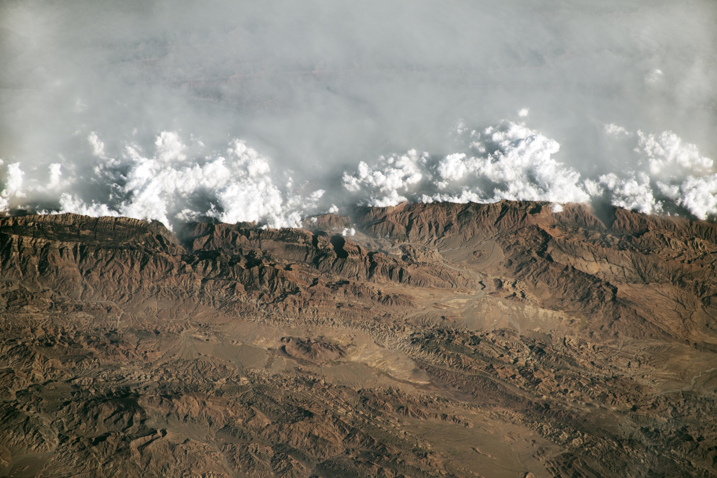 Astronaut photograph of clouds and haze meeting the high ridges of the Sulaiman Mountains in Pakistan.